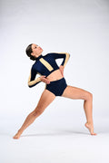 A woman in a navy blue and beige two-piece dance leotard poses dynamically in a lunge position against a seamless light gray studio background.
