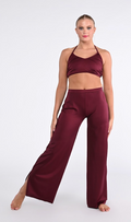 A woman modeling a matching two-piece dancewear set in deep burgundy, featuring a halter crop top and high-waisted wide-leg pants, against a plain light gray studio background.